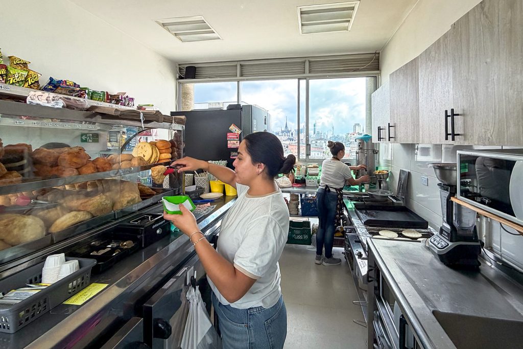 oven atiende una cafetería universitaria mientras prepara alimentos y bebidas en un espacio de trabajo informal en Colombia.